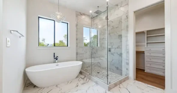 Luxurious bathroom with freestanding tub, marble tiling, large glass shower, and adjacent walk-in closet entryway.