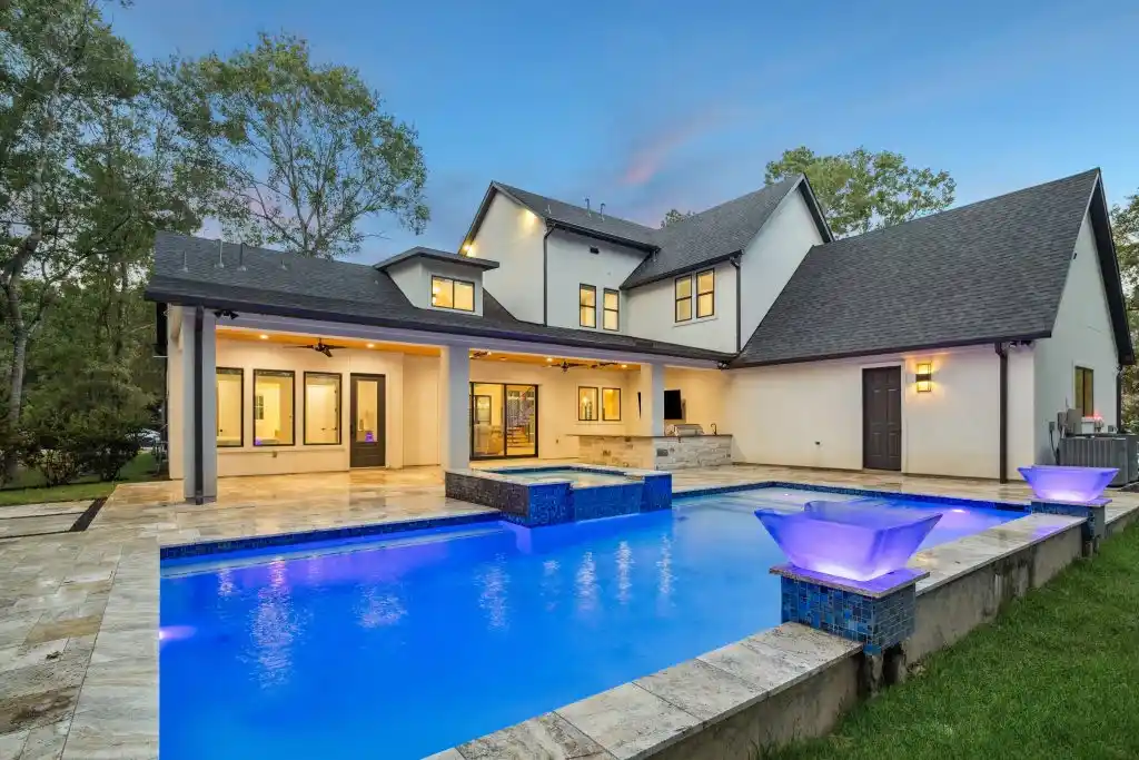 Luxury custom home at dusk featuring a glowing blue swimming pool, modern spa, and covered patio.