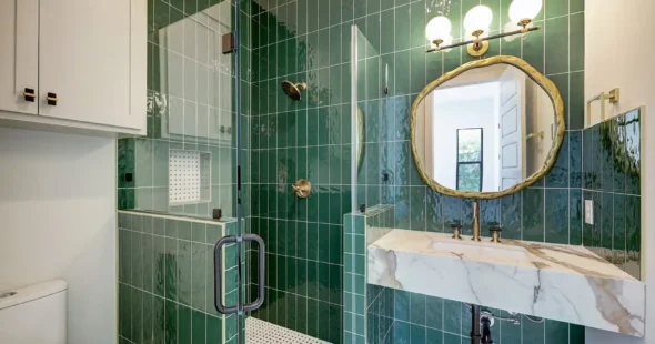 Emerald green tile bathroom with brass round mirror and marble vanity by Iconic Custom Home Builders
